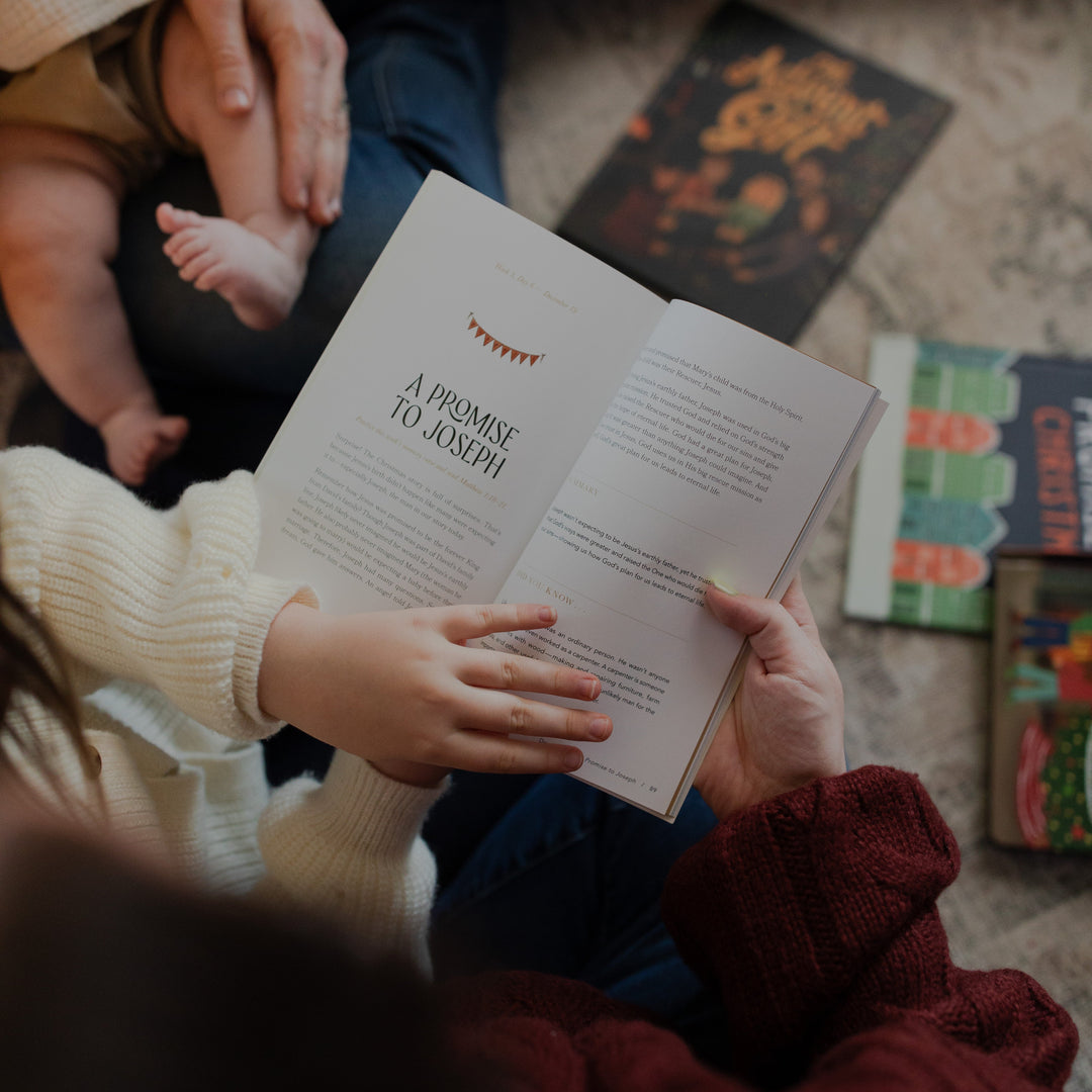 A woman and a child holding open the Advent Adventure Devotional with other Daily grace board books on the ground