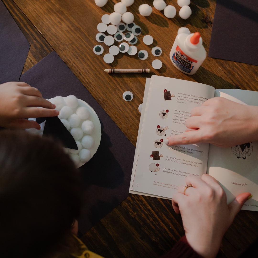 A woman pointing to a craft page in the Advent Adventure while a child has her hand in a plate of cotton balls.