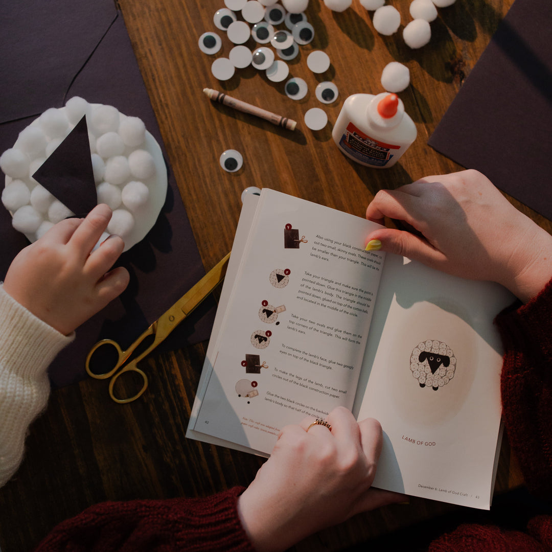 A woman is holding open the Advent Adventure devotional book with a child's hand in a plate of cotton balls