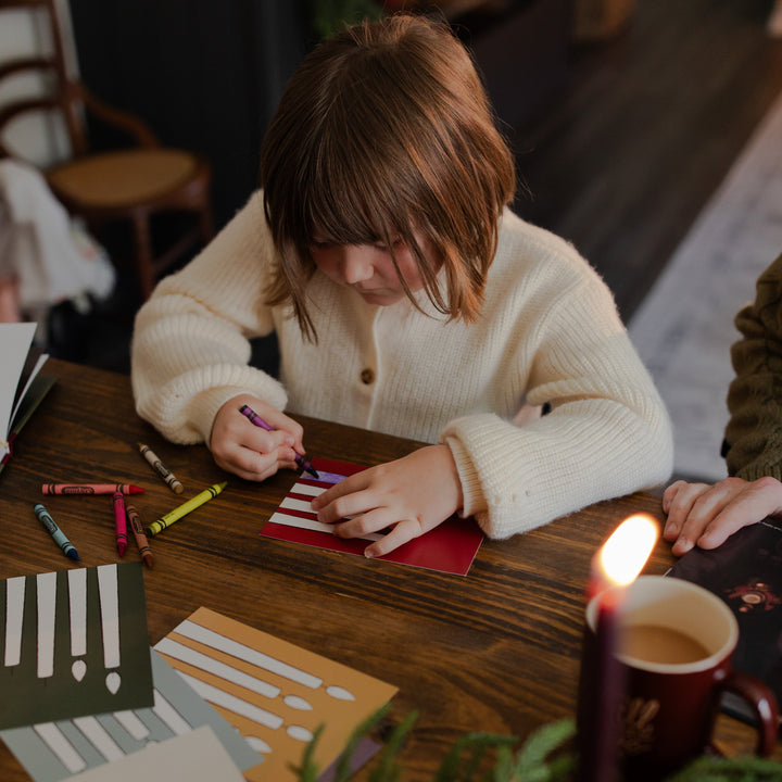A child sitting at a wooden table coloring in a Advent Adventure Candle Card