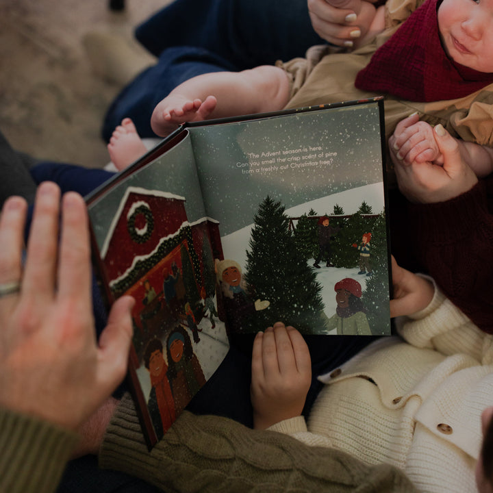Multiple people holding The Advent Gift book open while next to a baby