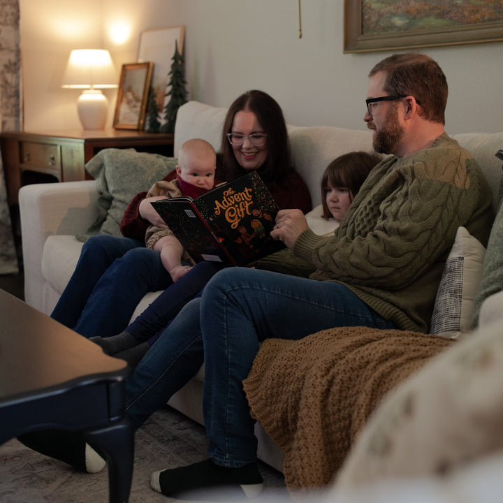 Family sitting on a couch in a living room reading The Advent Gift book together.