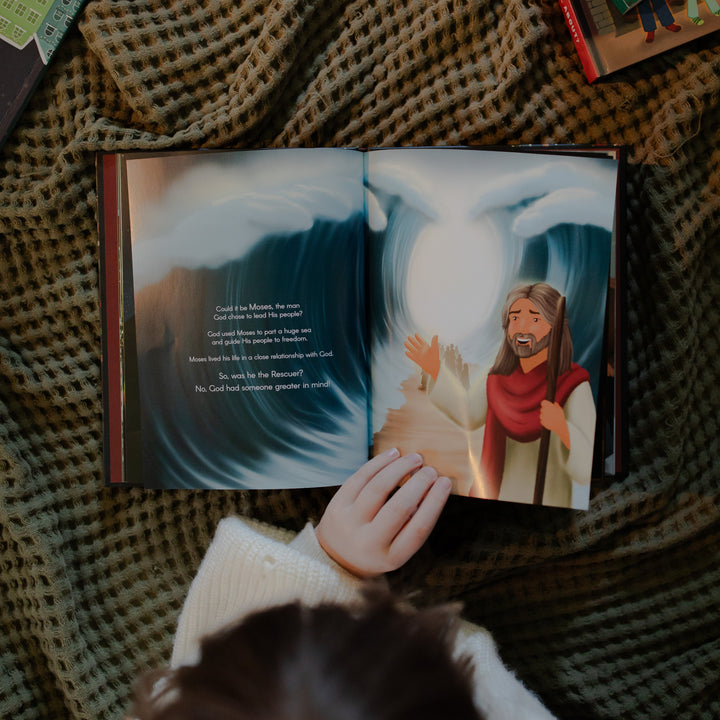 The Advent Gift Book opened with a child's hand resting on the page while laying on a textured blanket