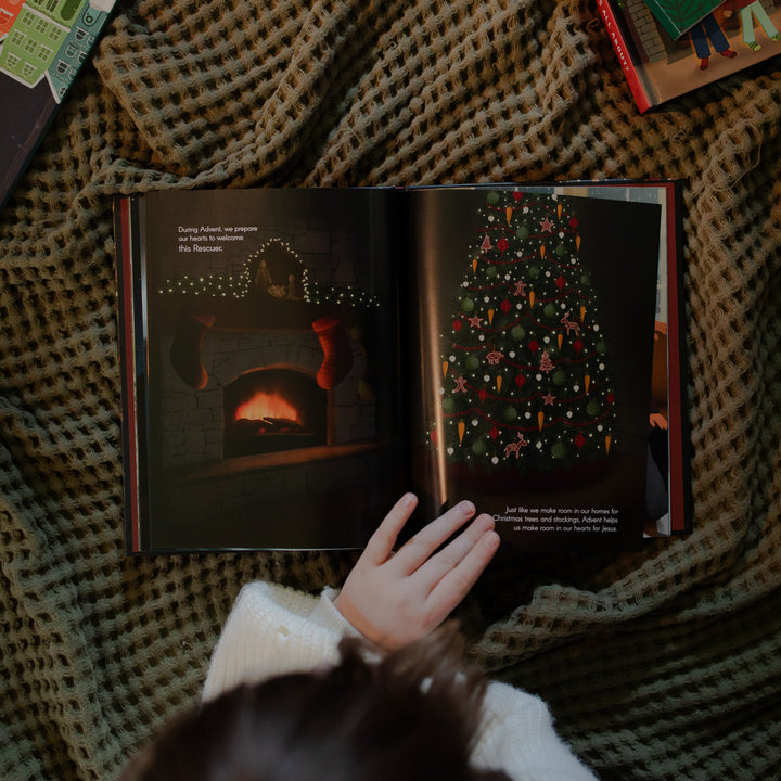 A child with their hand resting on The Advent Gift book page while on a textured blanket