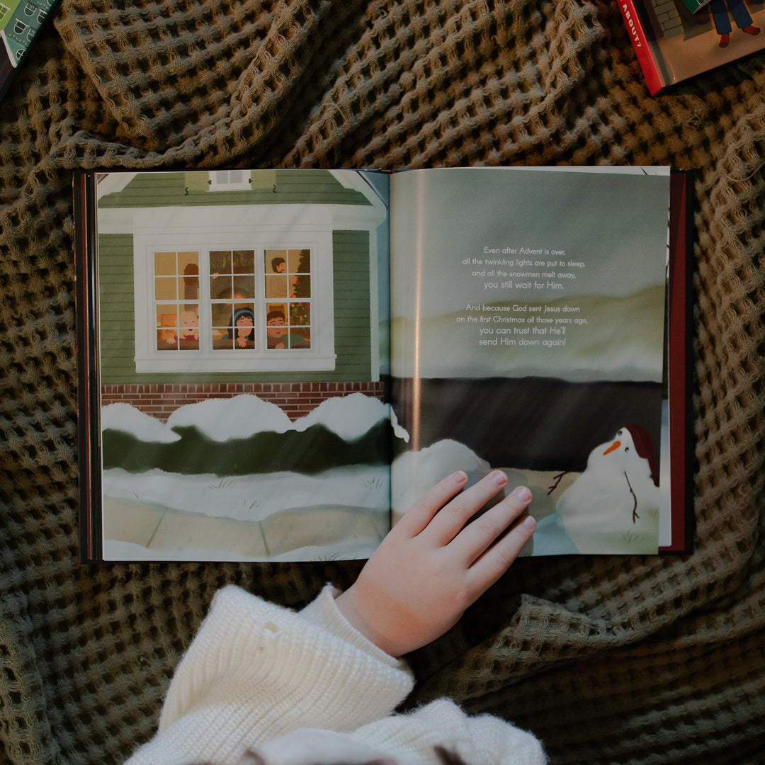 The Advent Gift book  opened to a snowy scene with a hand on the book