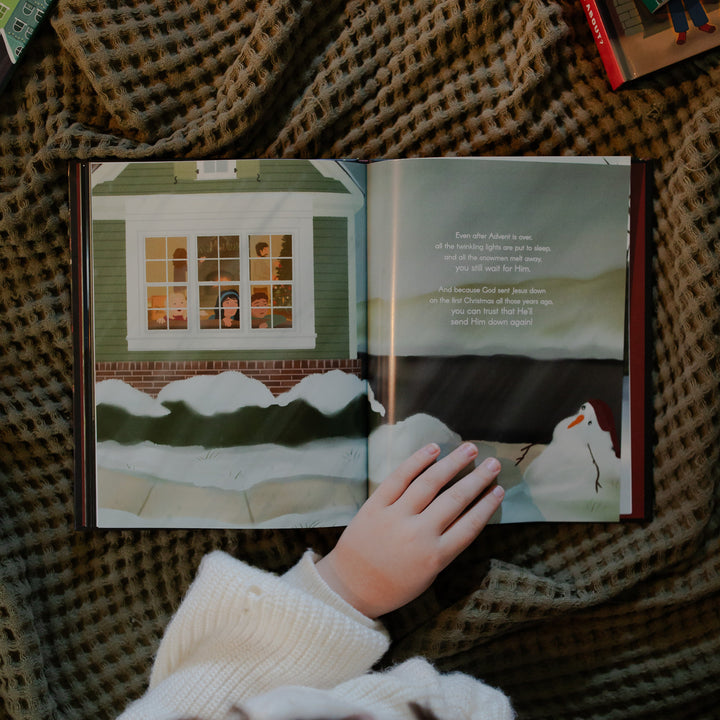 The Advent Gift book  opened to a snowy scene with a hand on the book