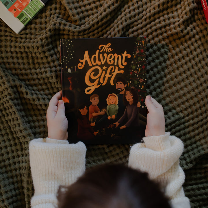 Person holding 'The Advent Gift' book with a checkered fabric blanket