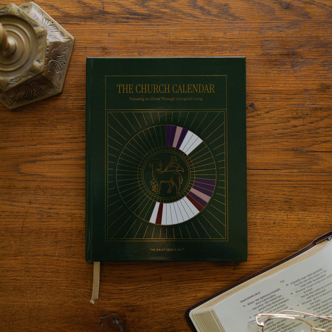 The Church Calendar cover laying on wooden table next an open bible and a bronze candlestick