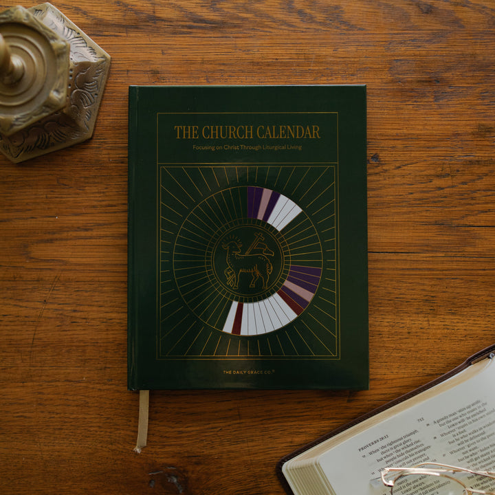 The Church Calendar cover laying on wooden table next an open bible and a bronze candlestick