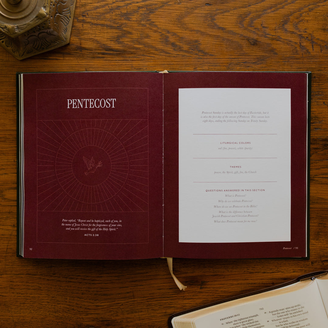 The Church Calendar opened to the Pentecost page laying on wooden table next an open bible and a bronze candlestick