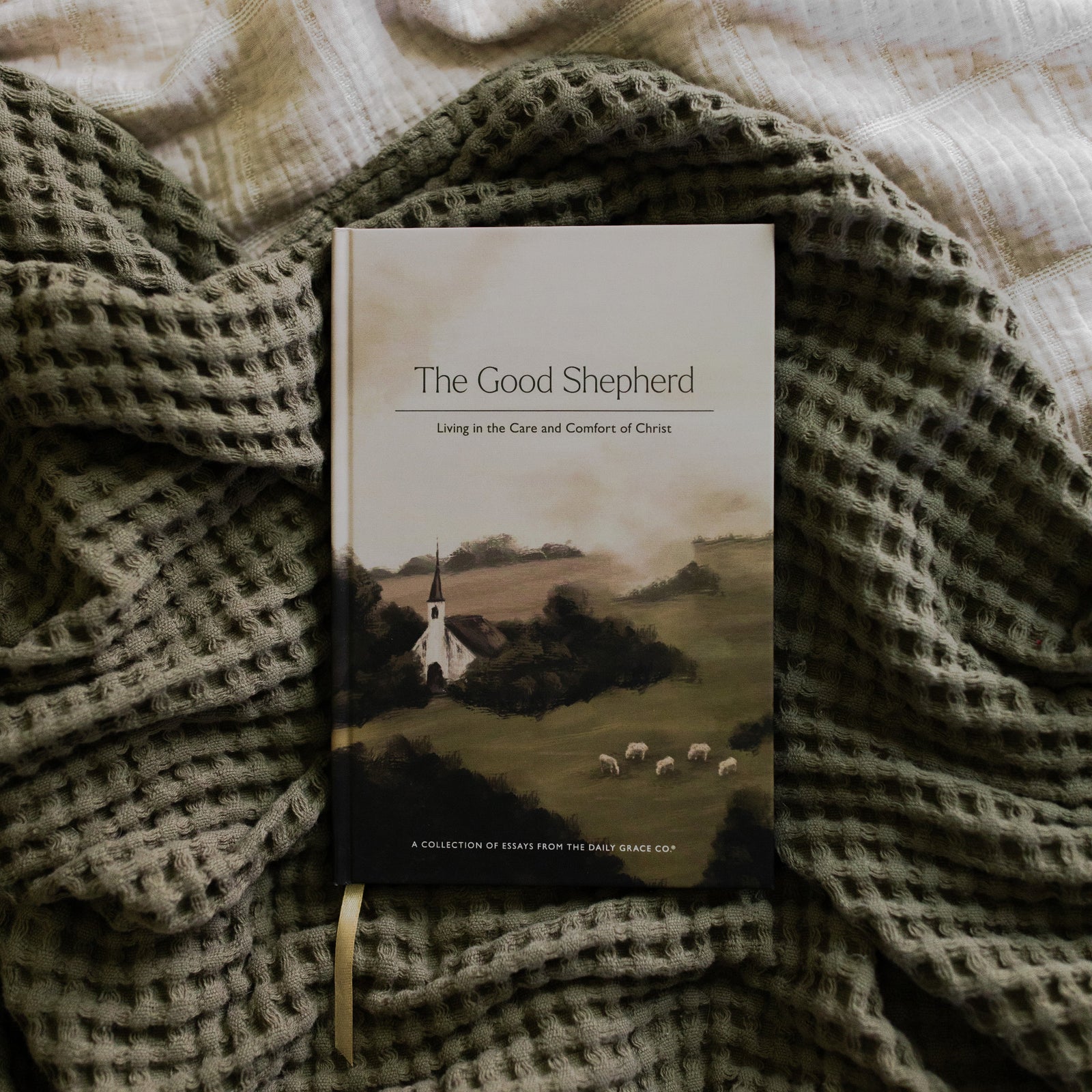 The Good Shepherd Cover laying on a green waffle styled blanket on another creme blanket