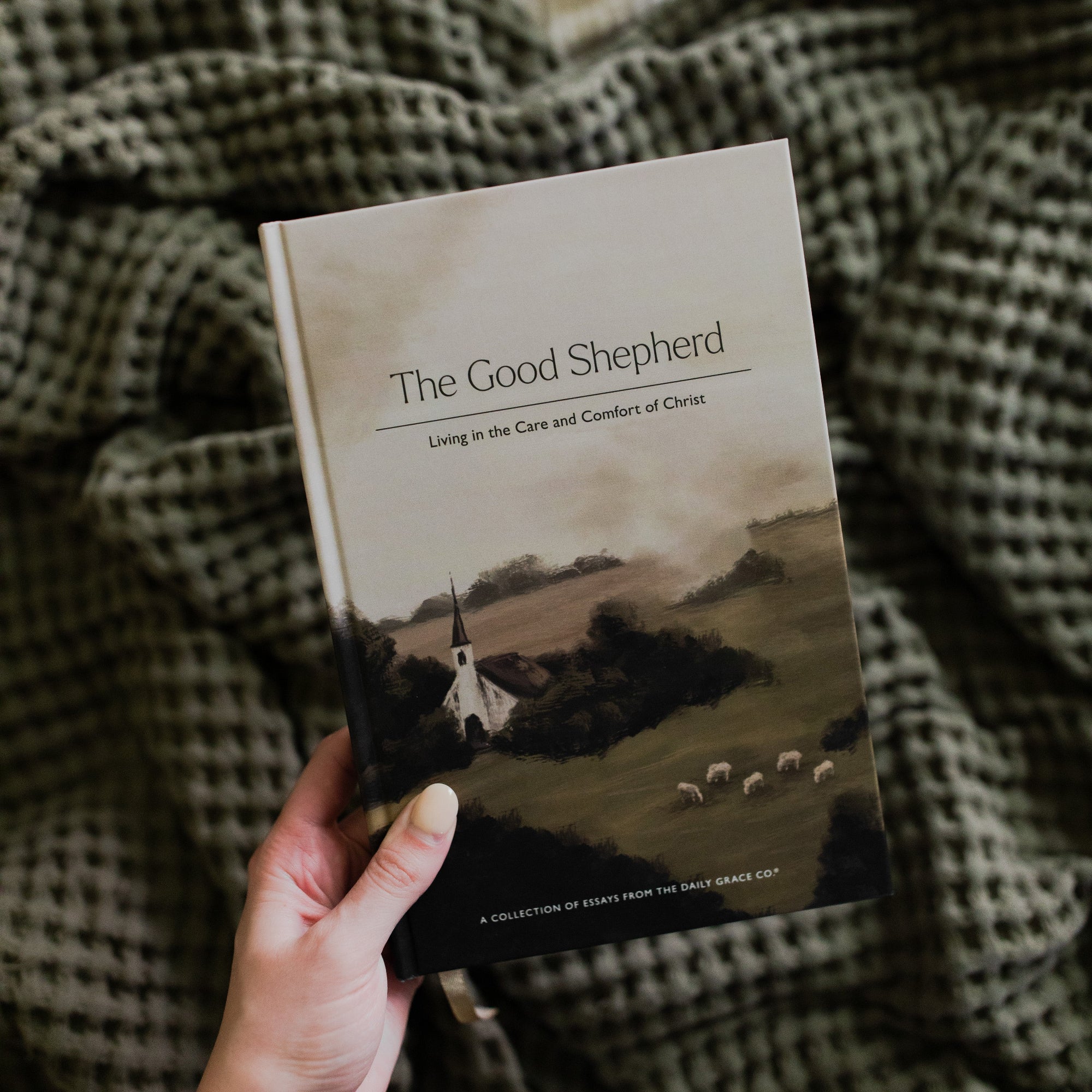 A Woman's hand holding The Good Shepherd Cover over a green waffle styled blanket