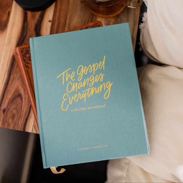 Book titled 'The Gospel Changes Everything' on a wooden surface with a cup of tea and a blanket.