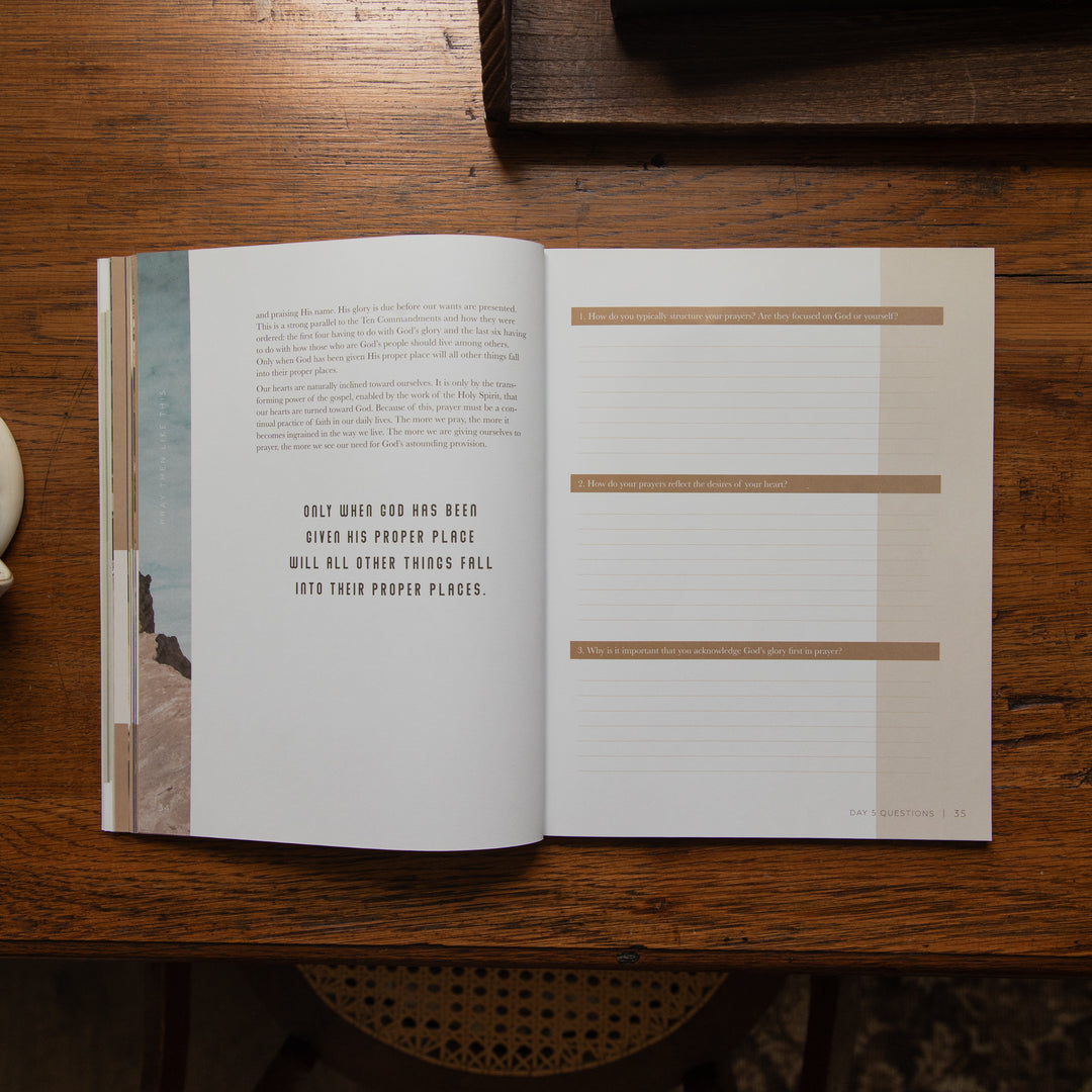 An open book lying on a dark wooden table, showing two interior pages with text and tan horizontal labels. The left page has a narrow vertical photo strip along the left edge, and the right page has lined writing space with headings.