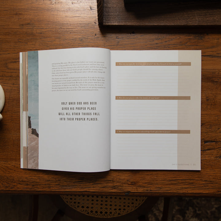 An open book lying on a dark wooden table, showing two interior pages with text and tan horizontal labels. The left page has a narrow vertical photo strip along the left edge, and the right page has lined writing space with headings.