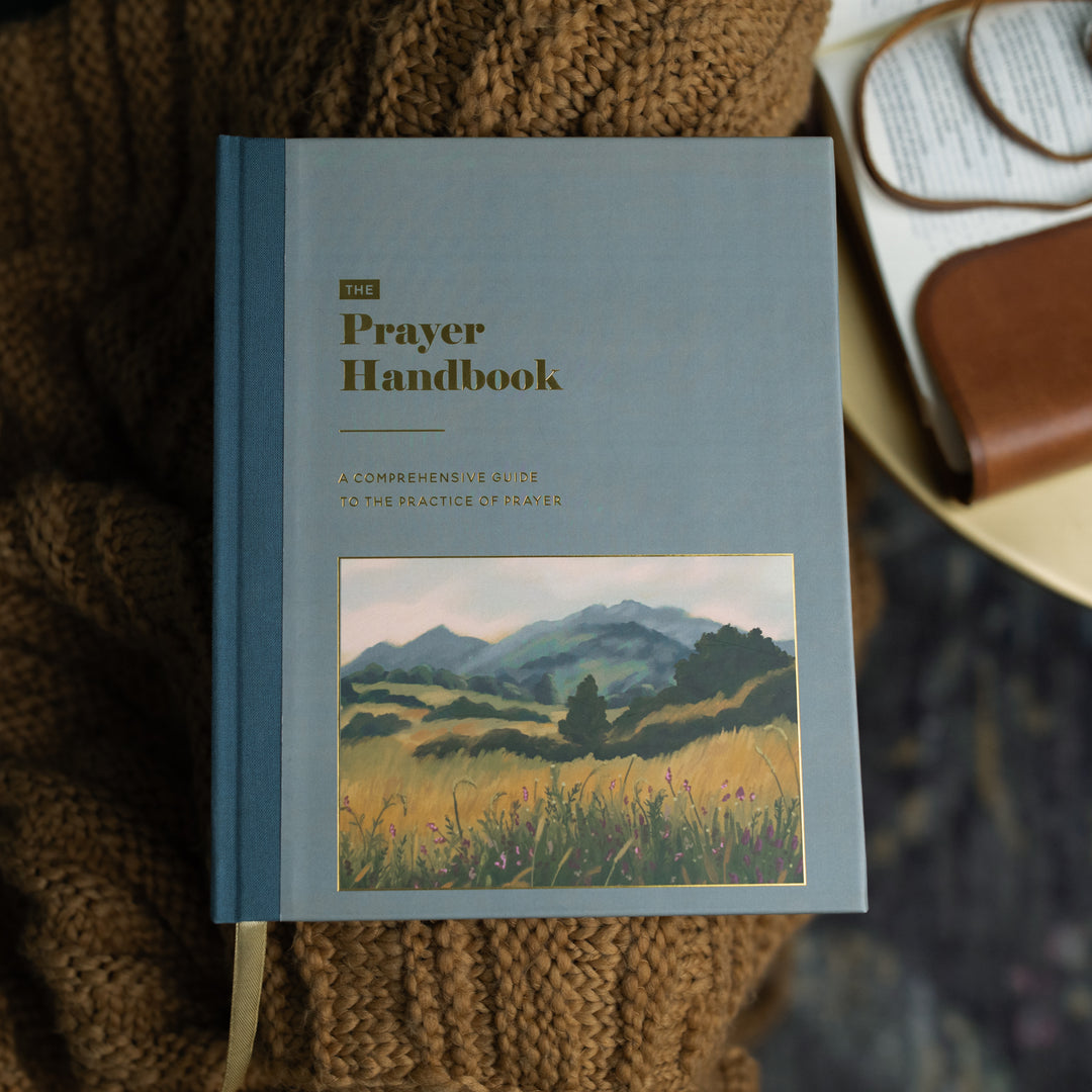 The Prayer Handbook cover on a brown knitted blanket next to a light wooden table
