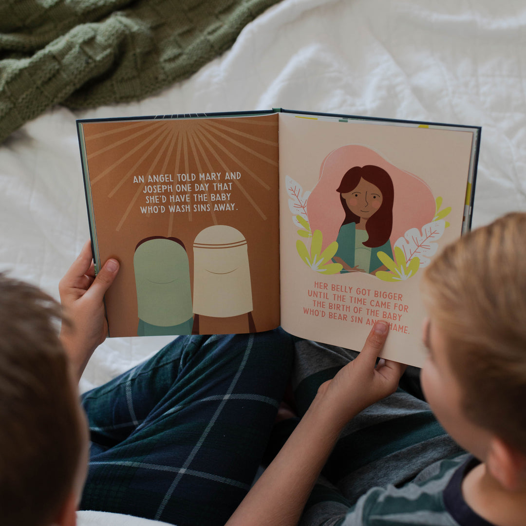 Two children reading the Promise of Christmas together on a bed.