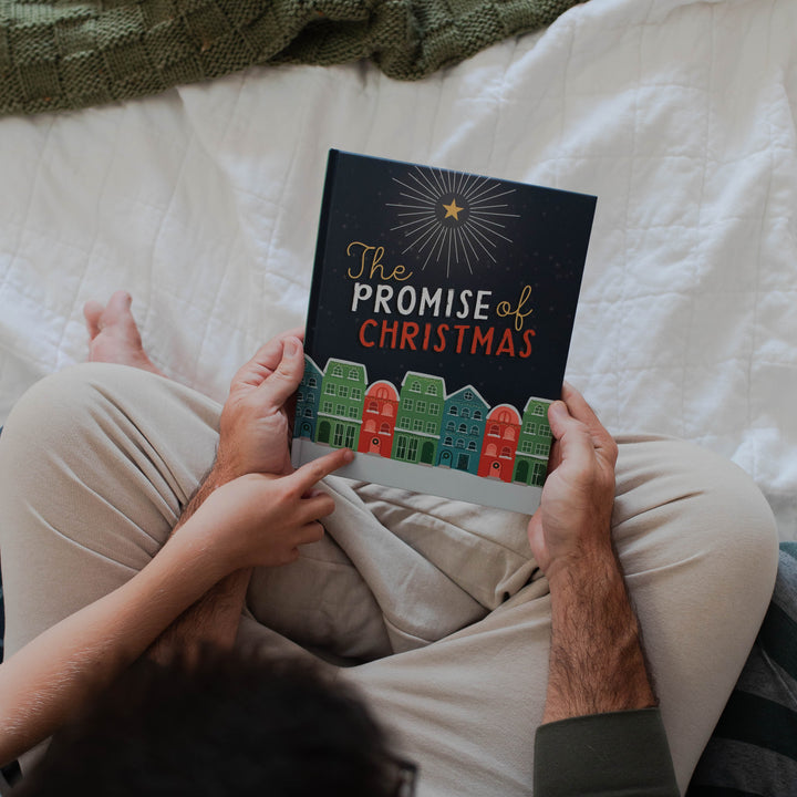 A father is holding The Promise of Christmas book while a child is pointing to the cover