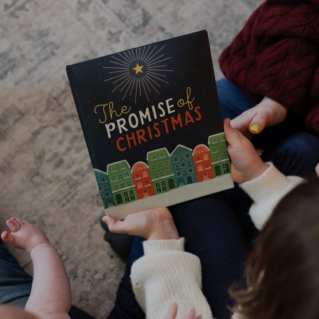 A child holding the cover of The Promise of Christmas next to a woman