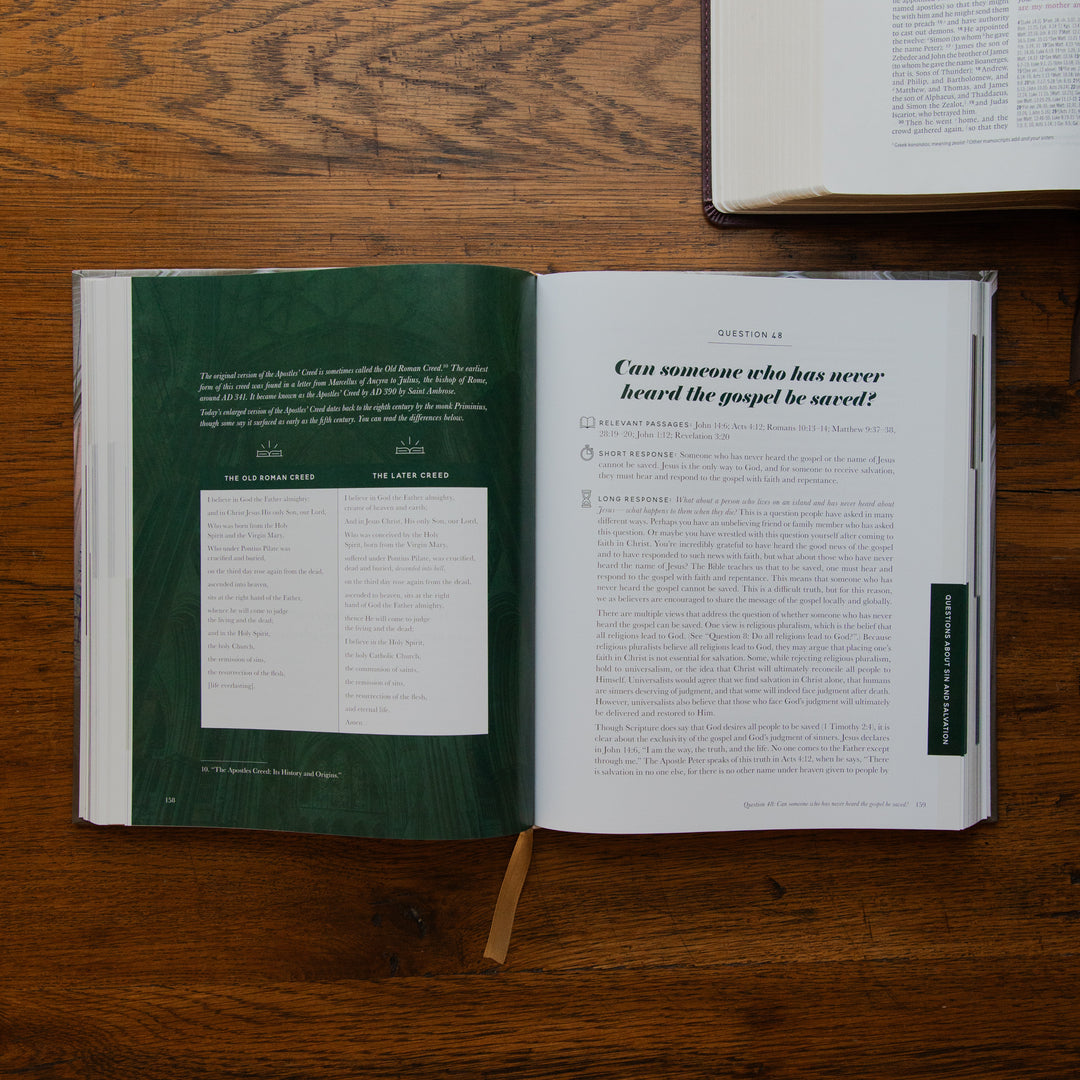 An open book spread laid on a wooden table, showing a dark green left page with text and a white right page with an article titled 'Can someone who has never heard the gospel be saved?'. Another book is partially visible at the top right.