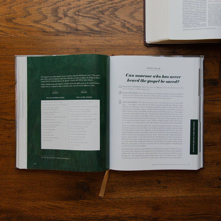An open book spread laid on a wooden table, showing a dark green left page with text and a white right page with an article titled 'Can someone who has never heard the gospel be saved?'. Another book is partially visible at the top right.