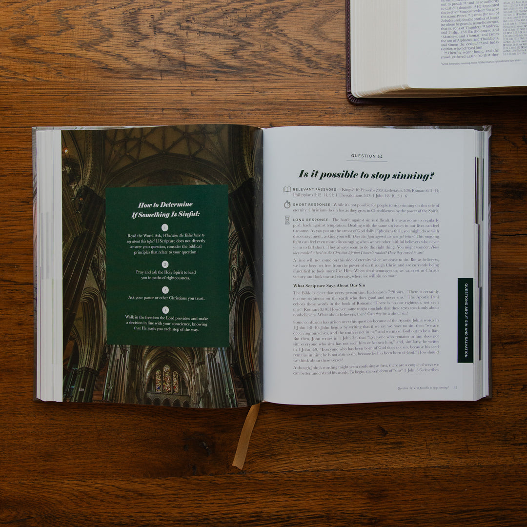 An open book laid flat on a wooden table, showing a printed interior page with a dark green panel containing steps and a question page with black text. A second book is partially visible at the top right.