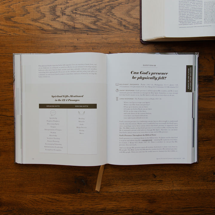 An open book spread laid on a wooden table, showing printed text and a bookmark ribbon. Another book is partially visible at the top right.