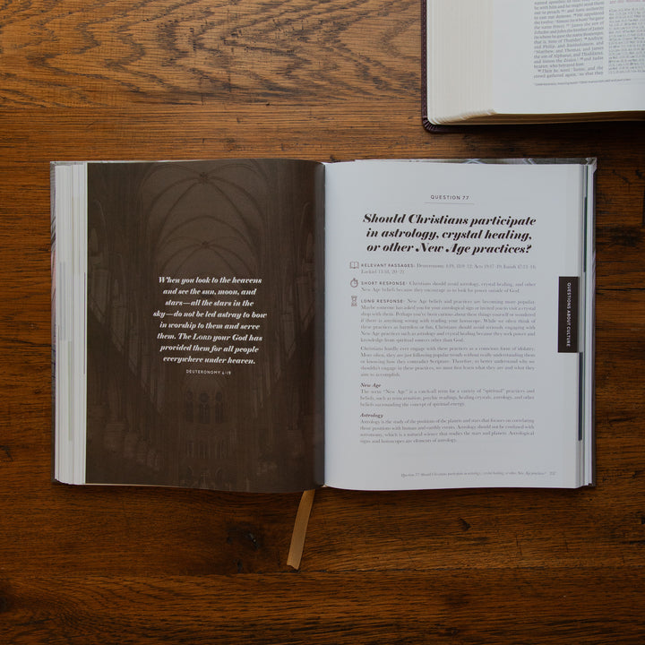 An open book laid flat on a wooden tabletop, showing a dark brown wood-textured left page with a quote and a white right page with printed text. A small bookmark hangs from the pages, and part of another book is visible at the top edge.