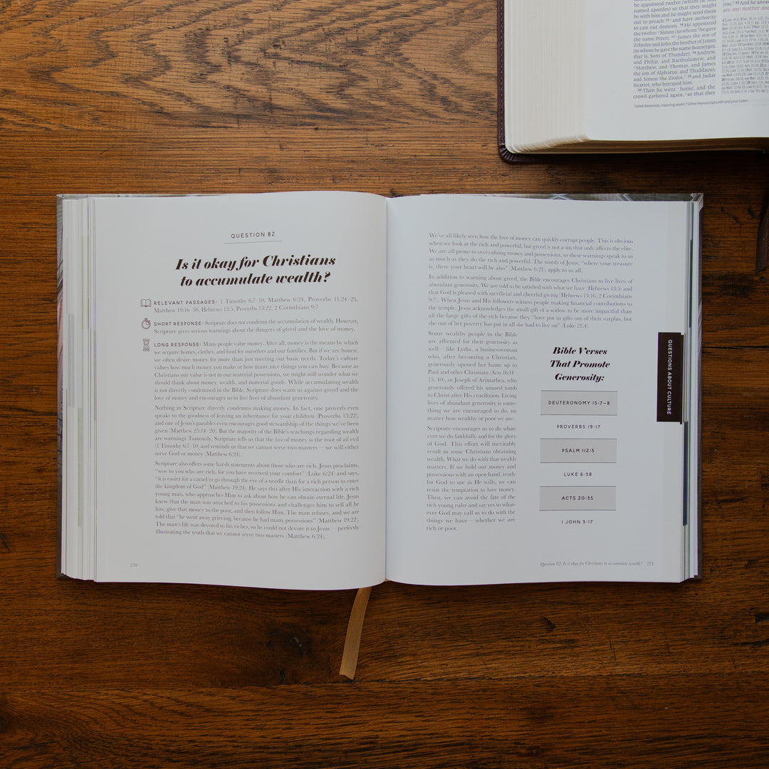 An open book with printed text laid on a wooden tabletop, with part of another book visible at the top right.