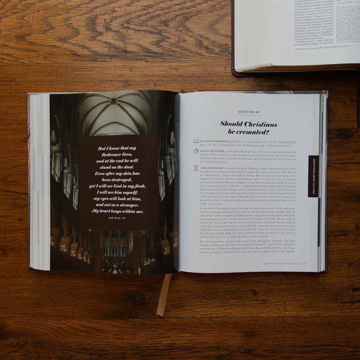 An open book laid flat on a wooden tabletop, showing a printed interior page with a poem over a dark photograph of a cathedral interior. Another open book is partially visible at the top right.