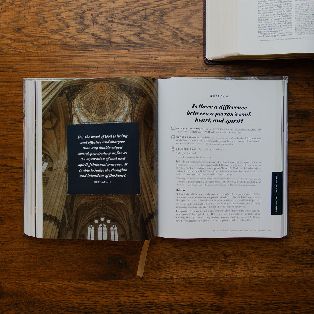 An open book lying on a wooden tabletop, showing a printed interior page with a cathedral interior photograph, a black text box, and a section titled 'Is there a difference between a person's soul, heart, and spirit!'. Another book is partially visible at the top right.