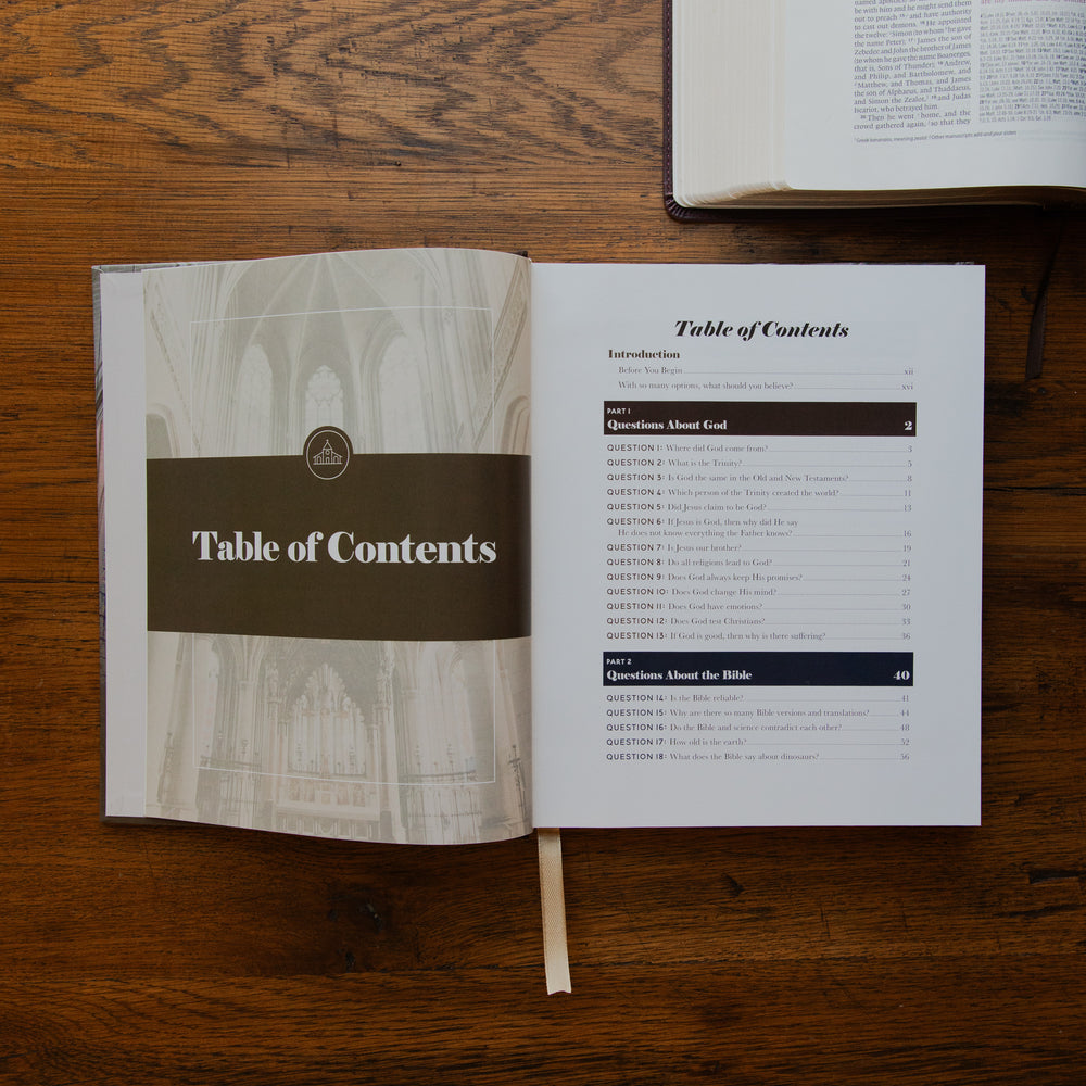 An open booklet showing the Table of Contents spread on a wooden tabletop, with another open book partially visible at the top right.