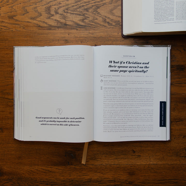 An open book laid flat on a wooden table, showing printed pages with a section titled 'What if a Christian and their spouse aren't on the same page spiritually?' A second book is partially visible at the top right.