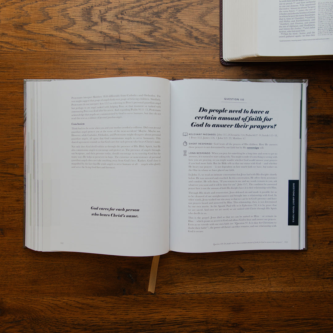 An open book laid flat on a wooden tabletop, showing printed text pages with a small bookmark ribbon protruding from the center. Another book is partially visible at the top edge.