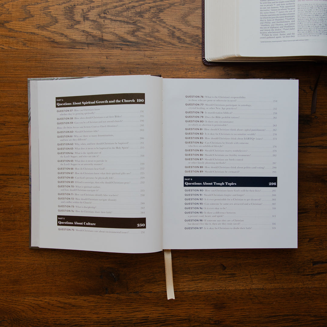 An open book showing printed pages with a table of contents, placed on a wooden tabletop. Another book is partially visible at the top right.