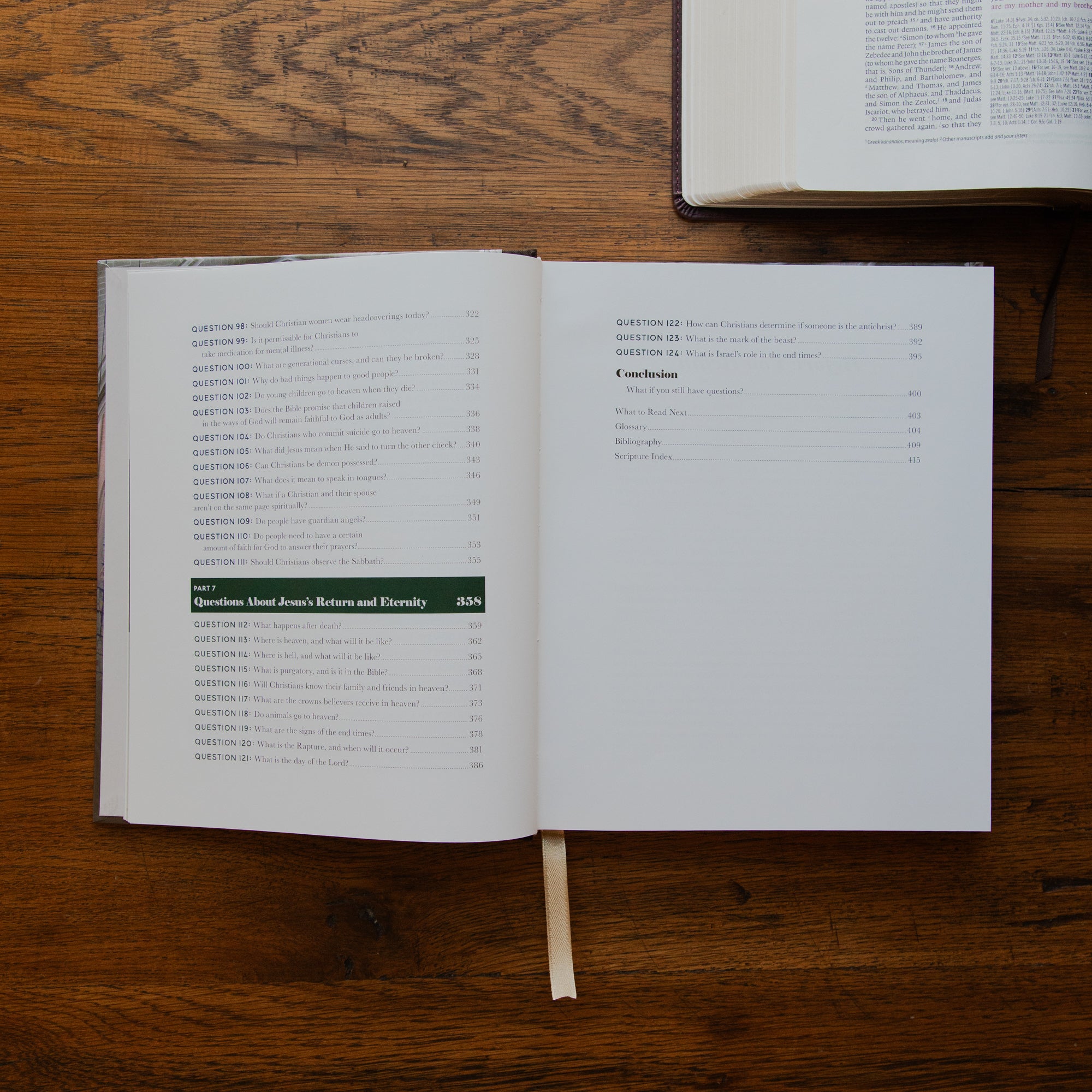 An open book showing printed text and a table of contents on a wooden tabletop, with another book partially visible at the top right.