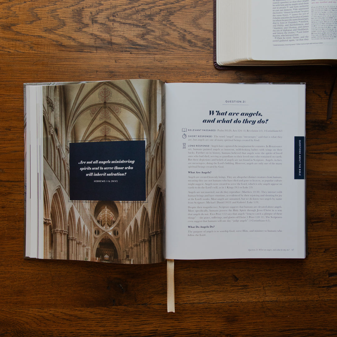 An open book laid flat on a wooden table, showing a printed interior spread with a cathedral interior photograph on the left page and a text page on the right. Another book is partially visible at the top right.