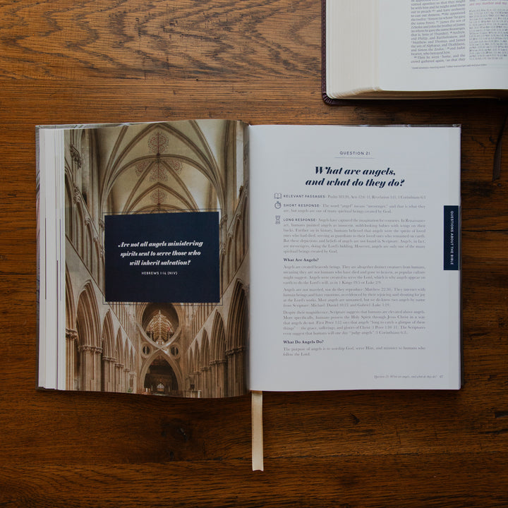 An open book laid flat on a wooden table, showing a printed interior spread with a cathedral interior photograph on the left page and a text page on the right. Another book is partially visible at the top right.