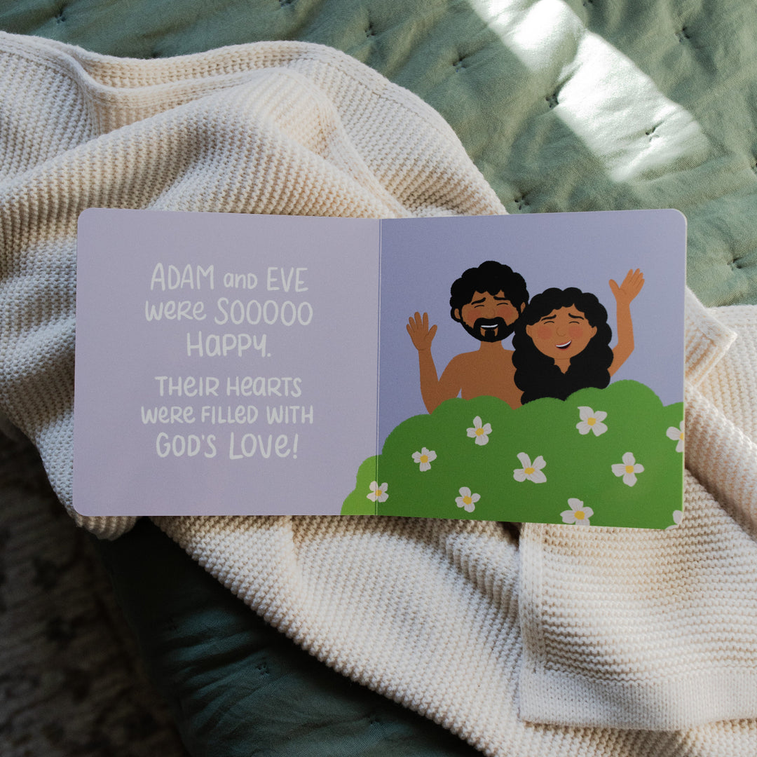 The Story of the Bible children's book opened to Adam and Eve's happiness laying on a white knitted blanket