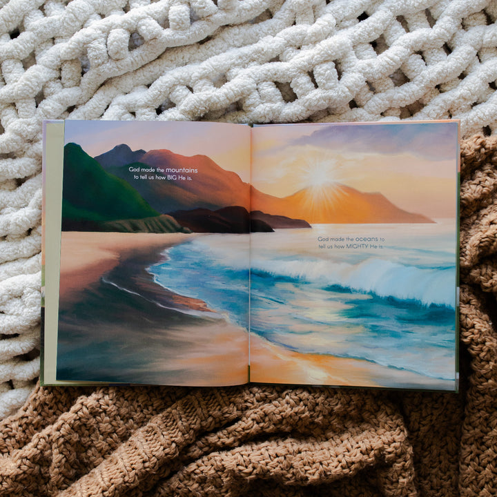 The Story of the Lost Sheep Book page of a beach side overlooking the waves next to a mountain landscape; the book is laying on multiple blankets, one brown and one cream colored