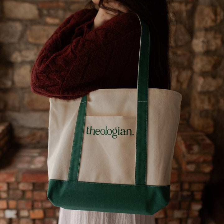 A woman with a red sweater holding a bag that says theologian on it over her shoulder