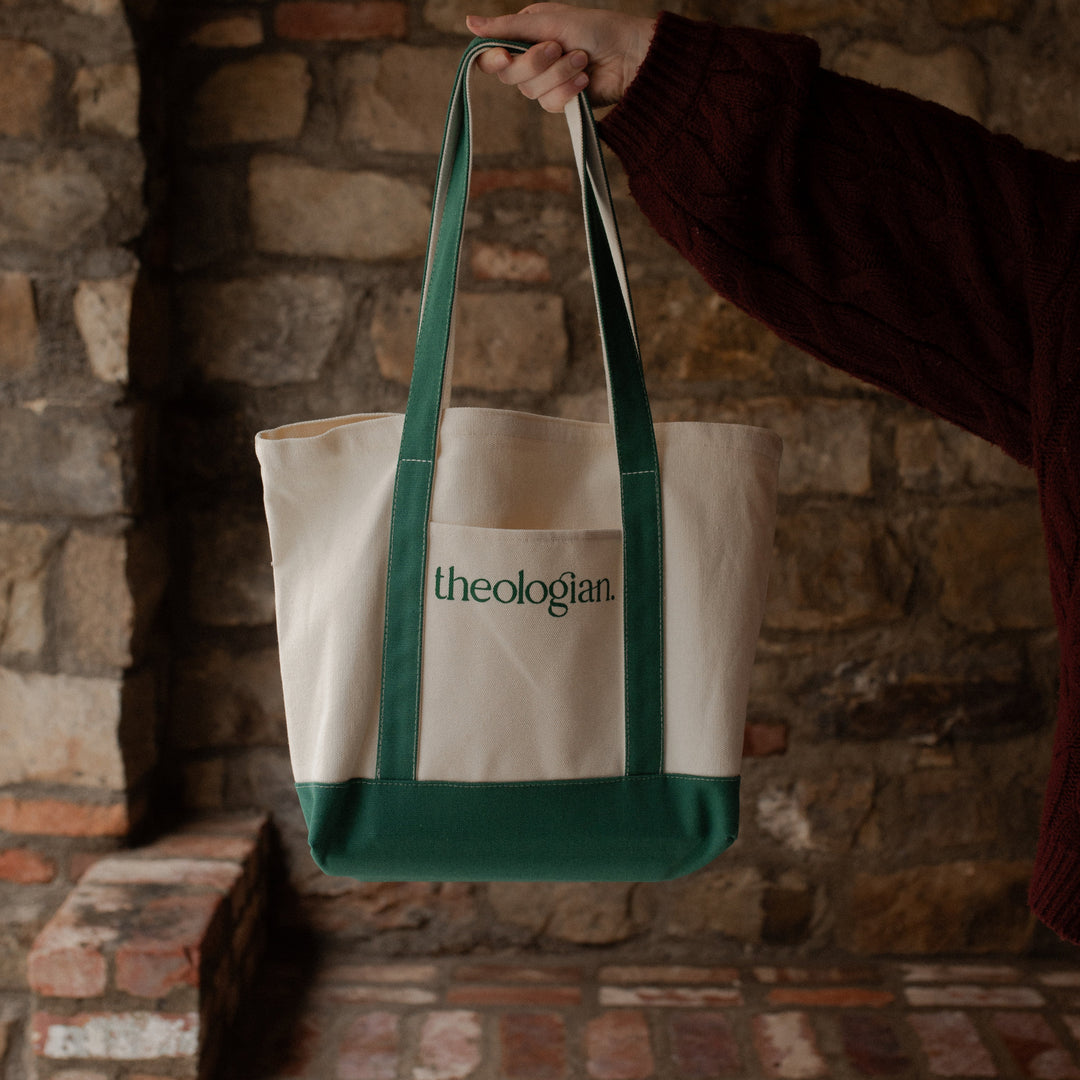 A woman with a red sweater holding a bag that says theologian on it near a brick wall