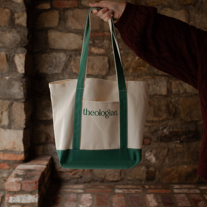 A woman with a red sweater holding a bag that says theologian on it near a brick wall