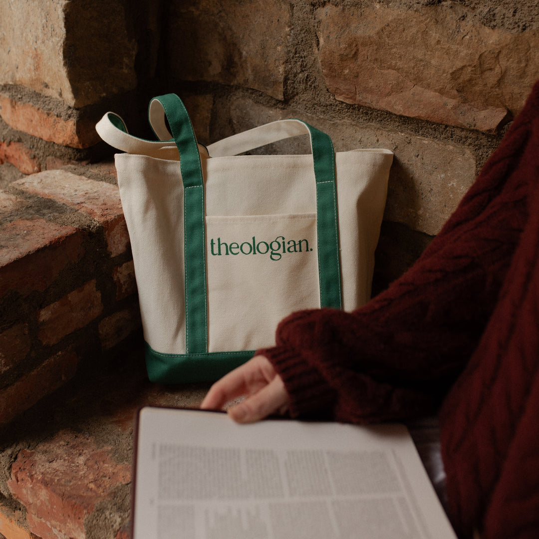 A woman with a red sweater next to a bag that says theologian on it on a brick bench