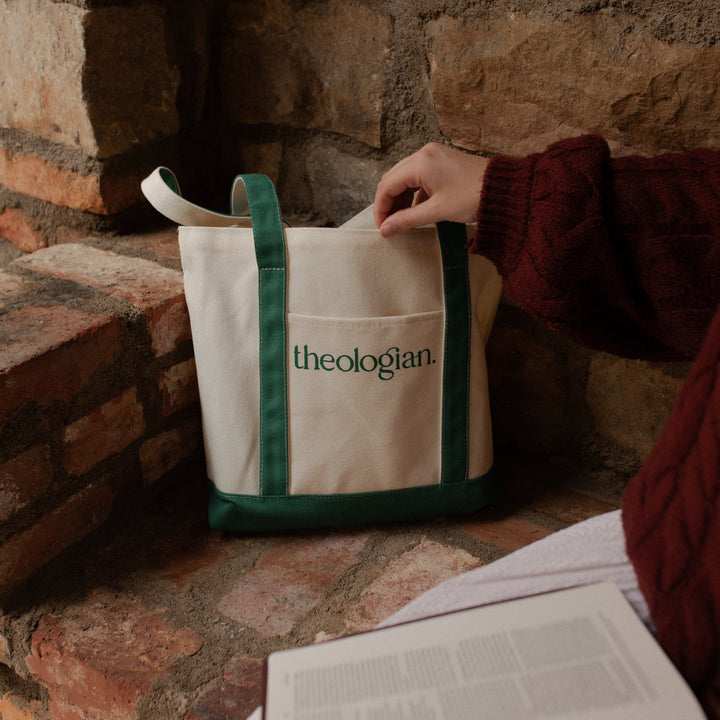 A woman with a red sweater touching a bag that says theologian on it on a brick bench