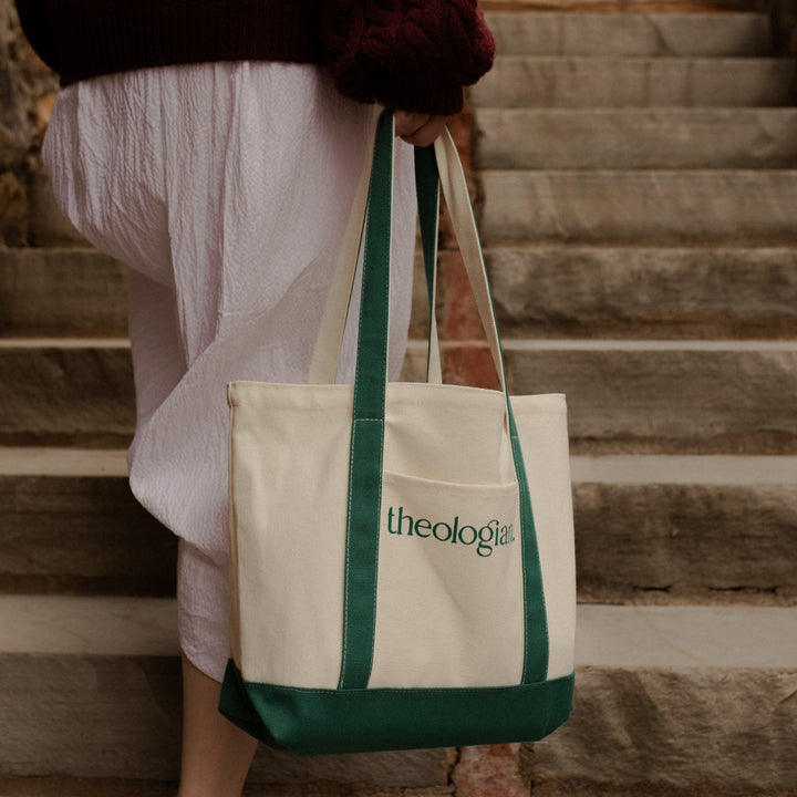 A woman with a white skirt walking up a set of stairs while holding a bag that says theologian on it