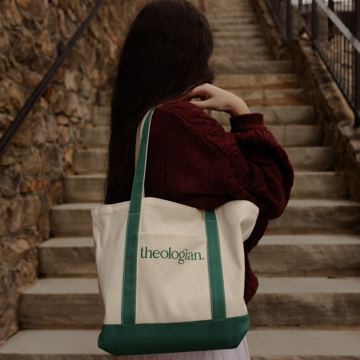 A woman facing toward a set of stairs while holding a bag that says theologian on it