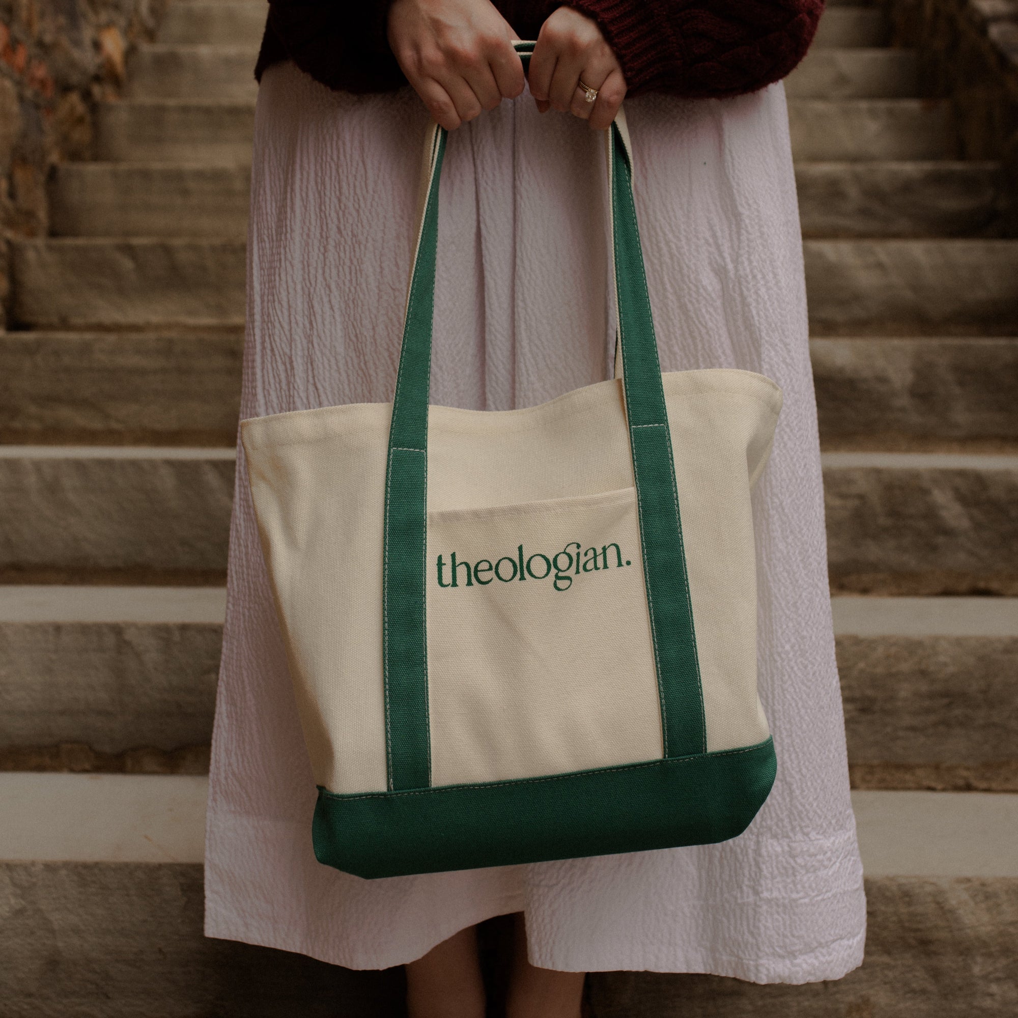 A woman on a set of stairs holding a bag that says theologian on it