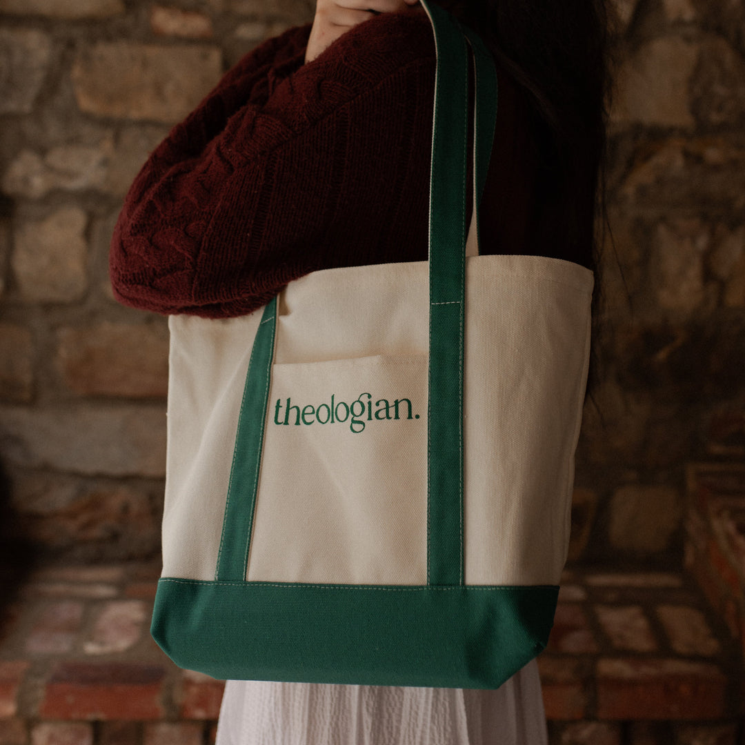 A woman with a red sweater holding a bag that says theologian on it over her shoulder while looking toward the camera direction