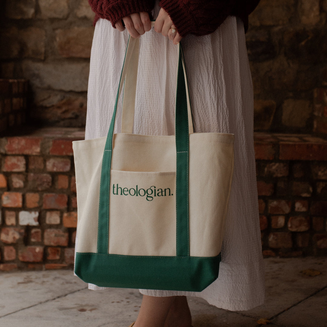 A woman with a red sweater and a white skirt holding a bag that says theologian on it